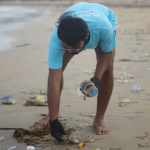 A photo of a male volunteer picking up trash from a littered beach.